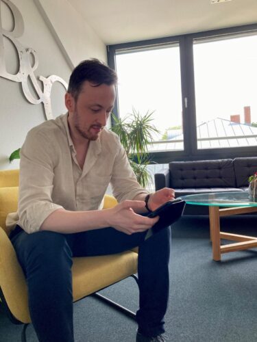 Radek sitzt auf einem gelben Stuhl und informiert sich auf seinem Smartphone über potenzielle Arbeitgeber